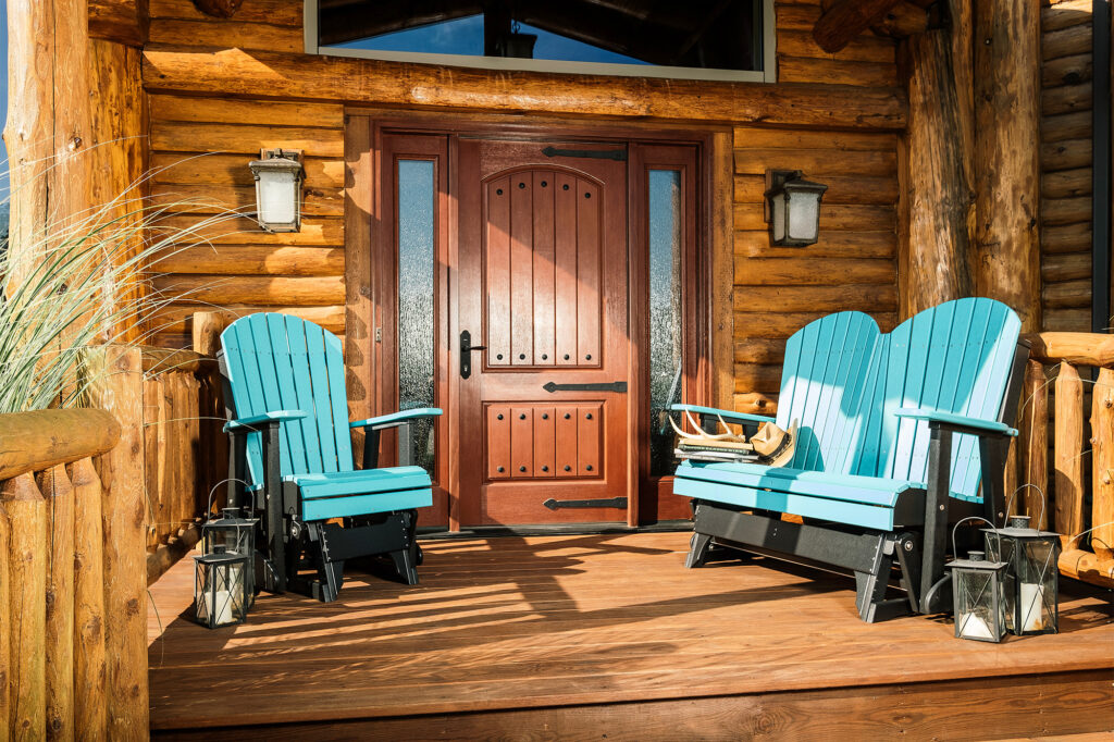 Amish made Aruba blue and black lawn furniture Adirondack glider chairs and loveseat on a rustic wooden porch, framed by a log cabin's entrance and lanterns.