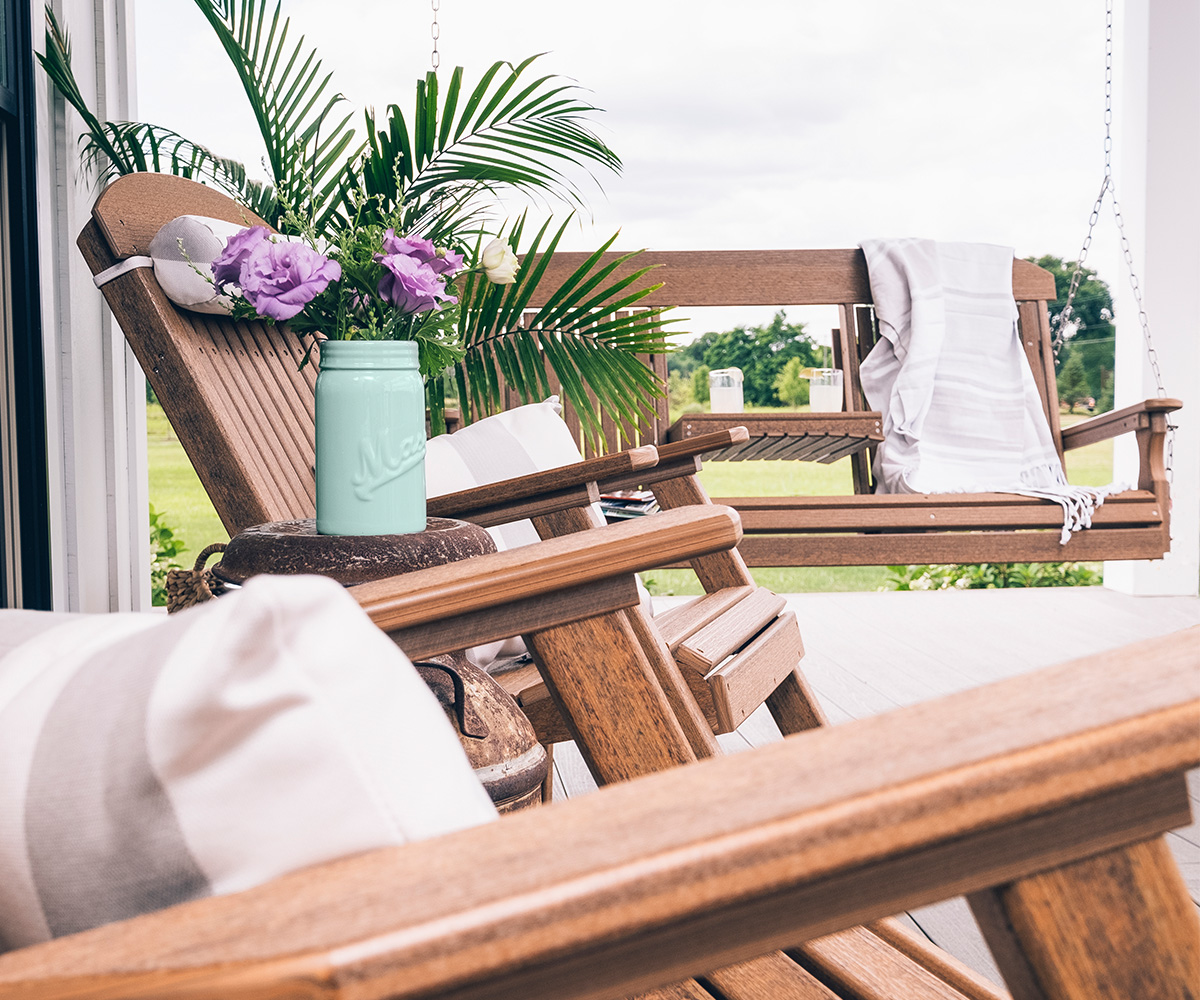 LuxCraft poly rocking chairs and porch swing with pillows and flowers on a sunny porch.