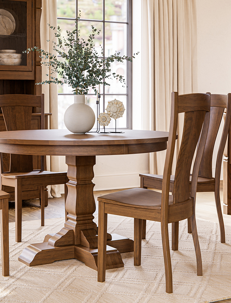 A handcrafted Amish dining set featuring a round pedestal table and matching wooden chairs in a warm cherry finish, placed in a bright, elegant dining room with classic decor. This furniture showcases the expert craftsmanship available at Amish stores in Hamptonville, NC.