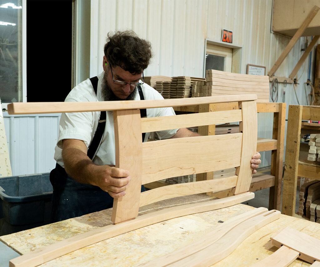 Craftsman assembling a hardwood bed frame, showing furniture building techniques in an Amish workshop