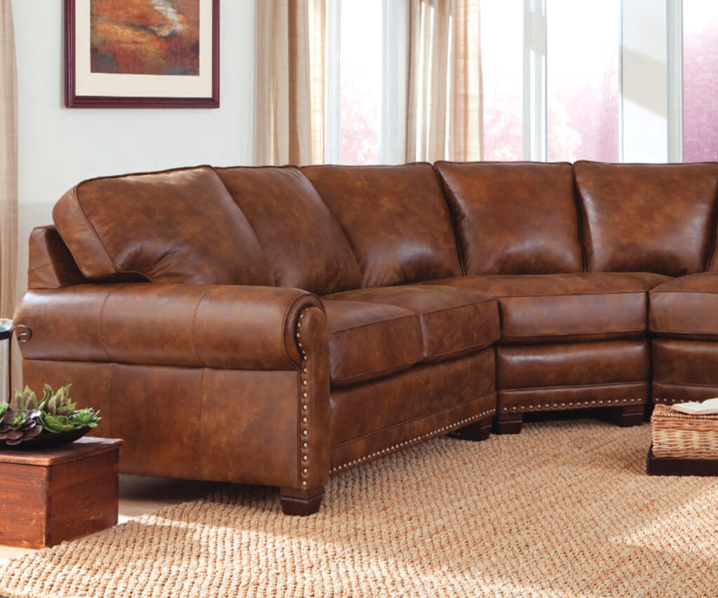 Brown leather sectional sofa with nailhead trim in bright living room with large windows.
