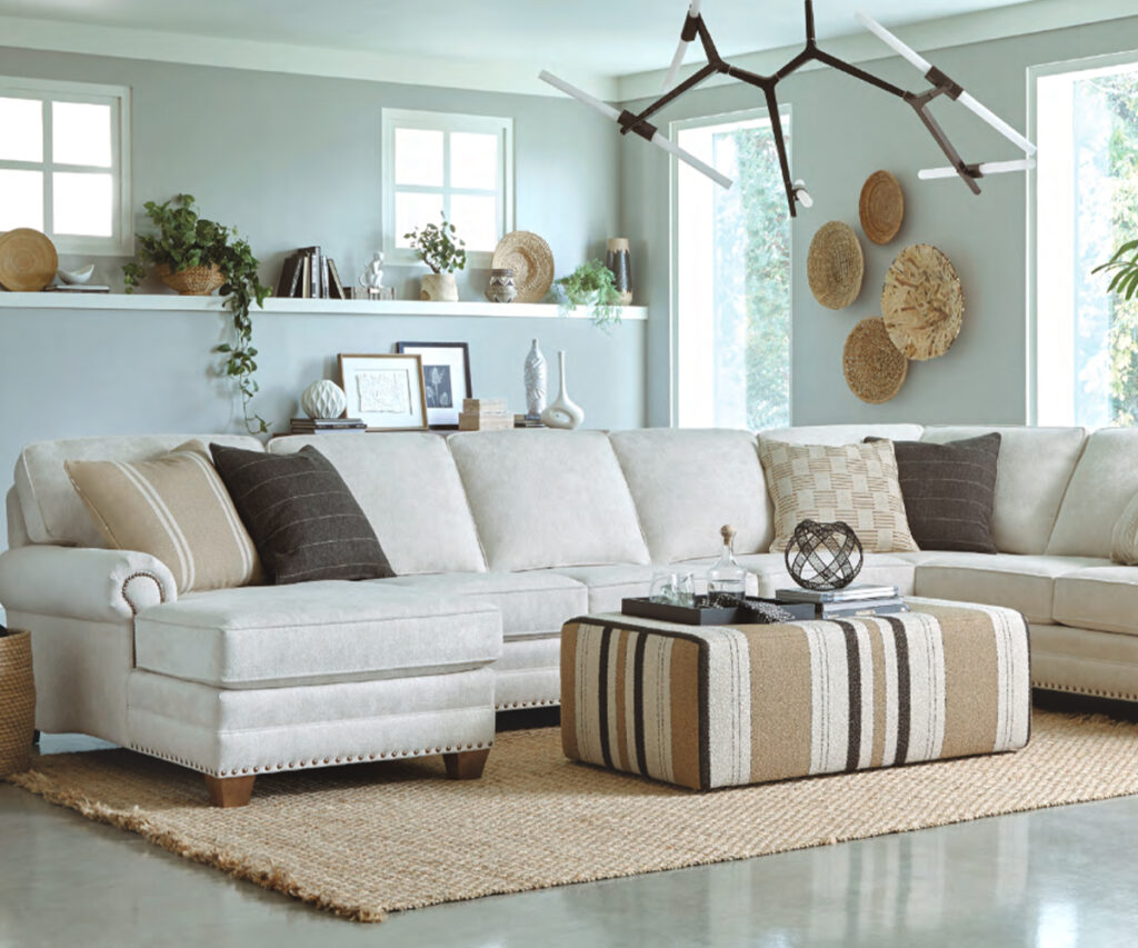 Light sectional sofa with ottoman and pillows in airy living room with plants.