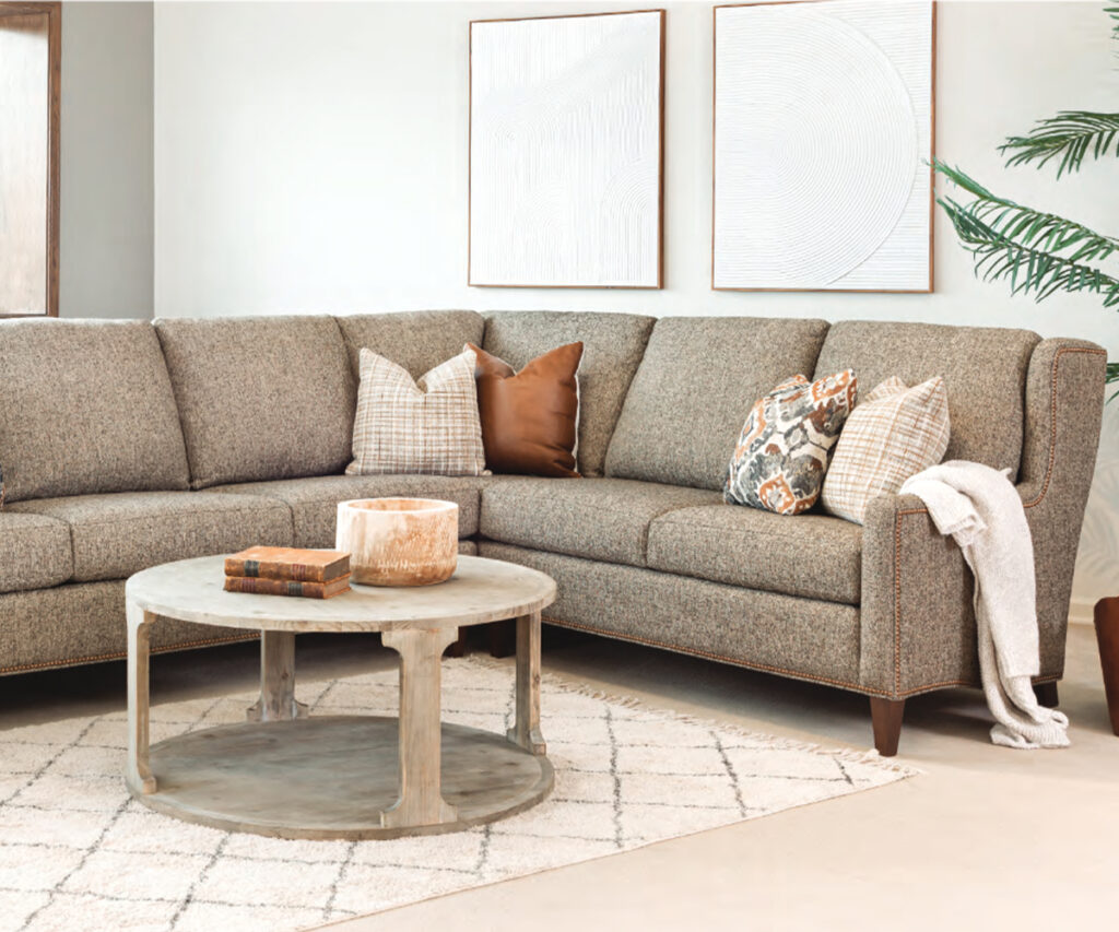 Neutral upholstered sectional sofa with pillows and round wood coffee table in bright living room.