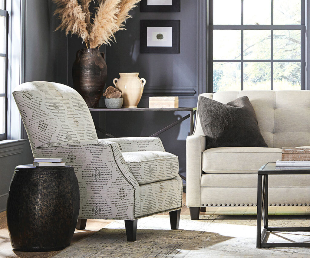 Upholstered accent chair and sofa in cozy living room with dark walls and window light.